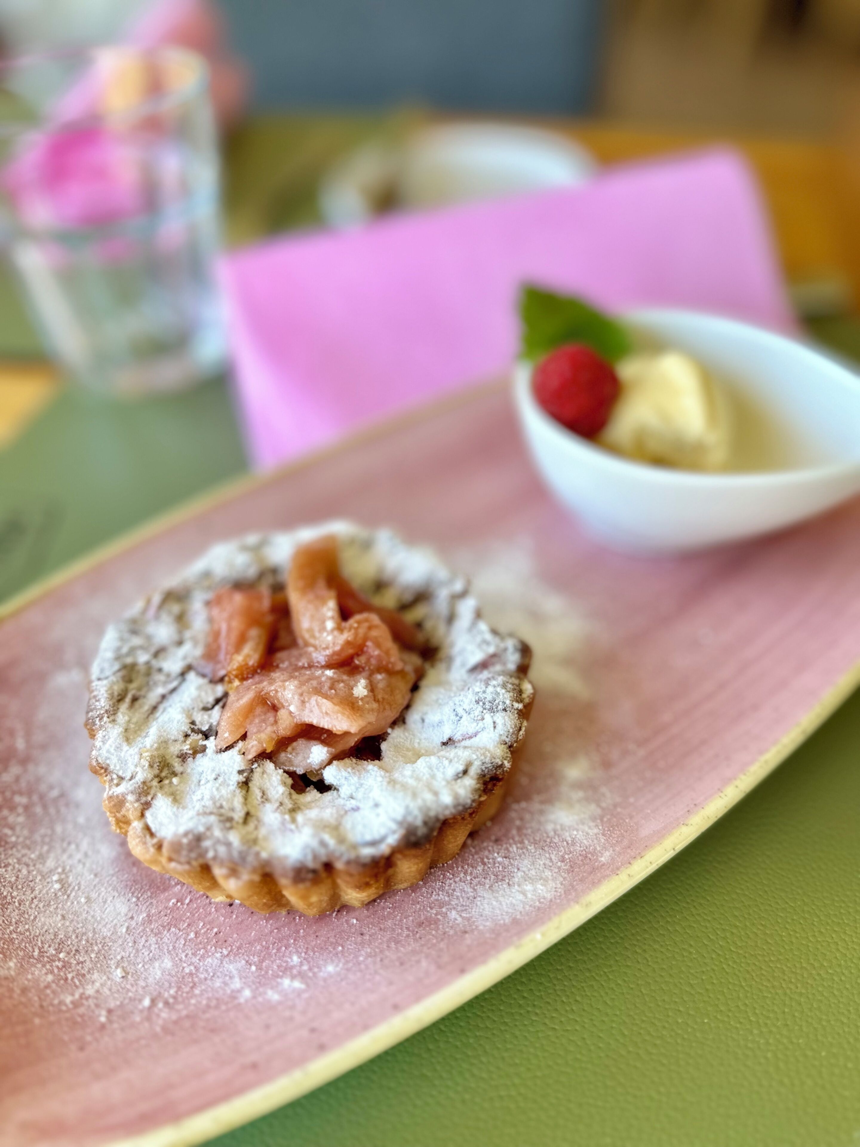 A dessert on a plate with powdered sugar, a berry, and a dollop of cream.