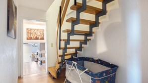 Eine Treppe mit Holzstufen und Metallgeländern, ein blaues Reisebett mit bunten Mustern und ein gerahmtes Bild an der Wand.