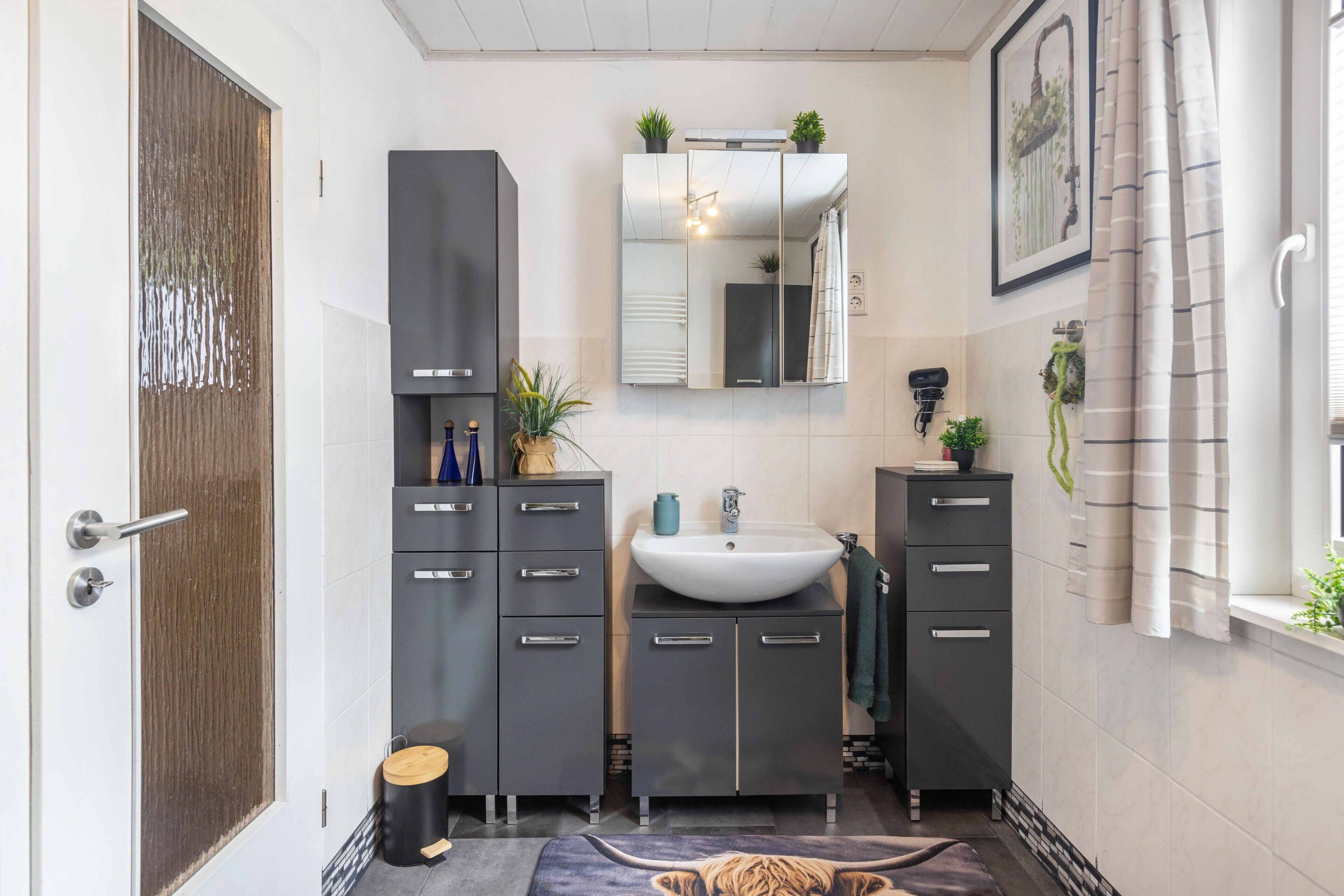 Une salle de bain moderne avec un grand miroir, un lavabo et deux armoires.