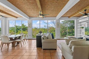 A spacious room with a dining table, chairs, a sofa, and a ceiling fan. - Villa Serenidad | Oceanview Pool Retreat (Rincón)