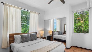 A bedroom with a bed, two bedside tables, a mirror, and a window with curtains.