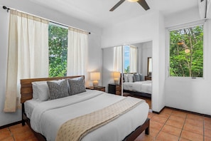 A bedroom with a bed, two bedside tables, a mirror, and a window with curtains. - Villa Serenidad | Oceanview Pool Retreat (Rincón)