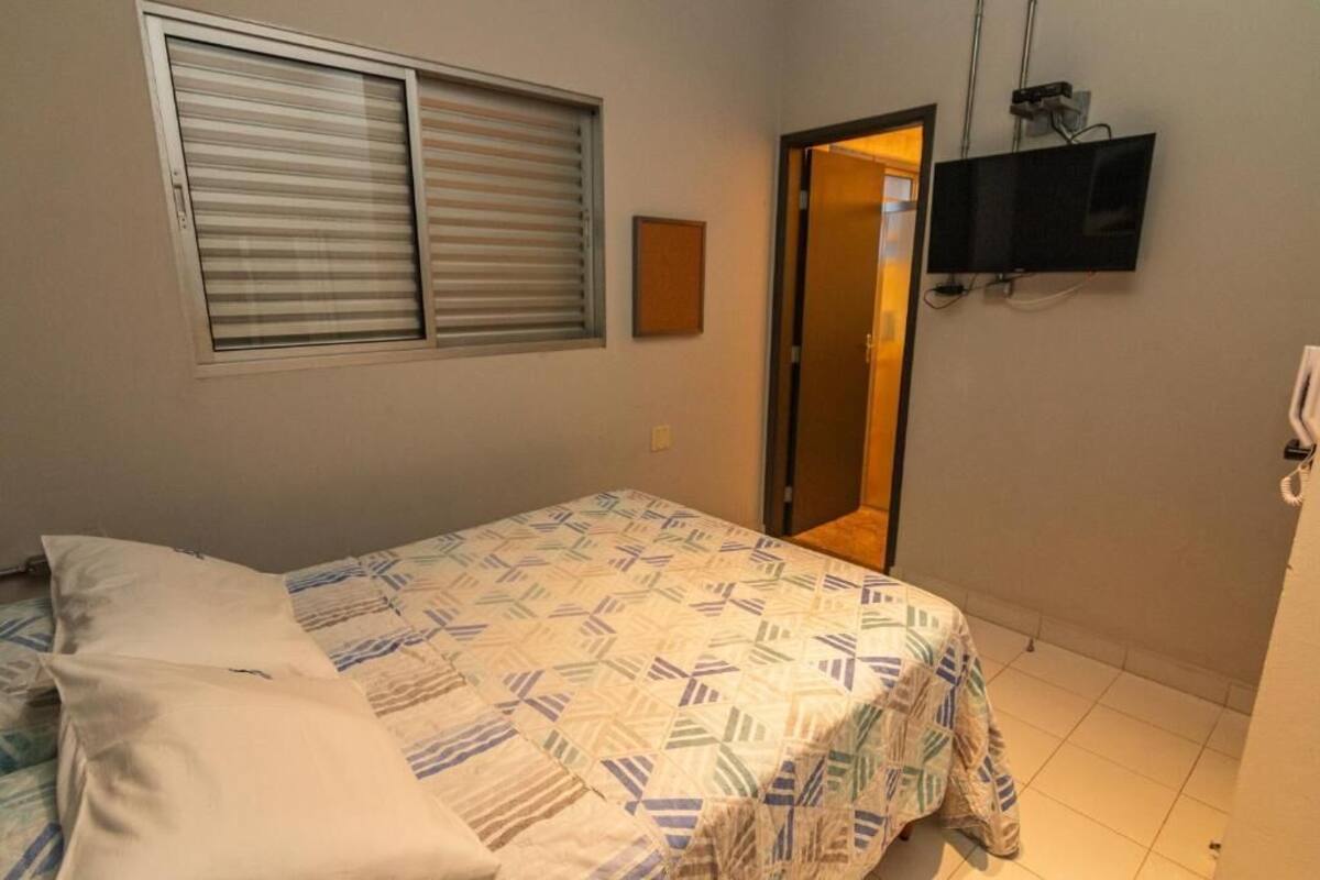 A bedroom with a bed, a television mounted on the wall, and a door leading to another room.