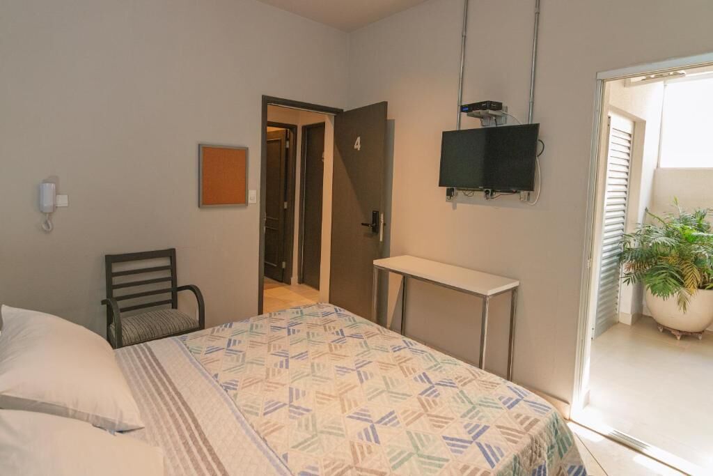 Une chambre à coucher comprenant un lit, une chaise, un bureau, un téléviseur et une porte donnant sur une autre pièce.