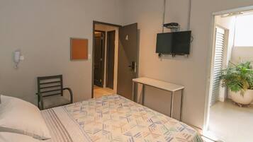 Une chambre à coucher comprenant un lit, une chaise, un bureau, un téléviseur et une porte donnant sur une autre pièce.