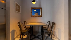 Un coin repas comprenant une table et quatre chaises, un luminaire suspendu, un tableau encadré et un interrupteur fixé au mur.