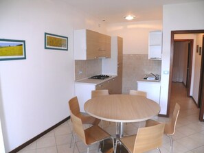 A compact kitchen with a round dining table and chairs, a small stove, and cabinets. - Holiday Home With Parking and Garden in Bibione (San Michele al Tagliamento)