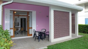 Un edificio moderno con fachada rosa, un patio cubierto con mesa y sillas, y una zona de cocina visible.