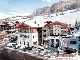 Una località turistica innevata con edifici in legno, un'area di parcheggio e una pista da sci sullo sfondo.