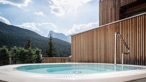 Una vasca idromassaggio con vista sulle montagne, rivestita in legno e con gradini in pietra.