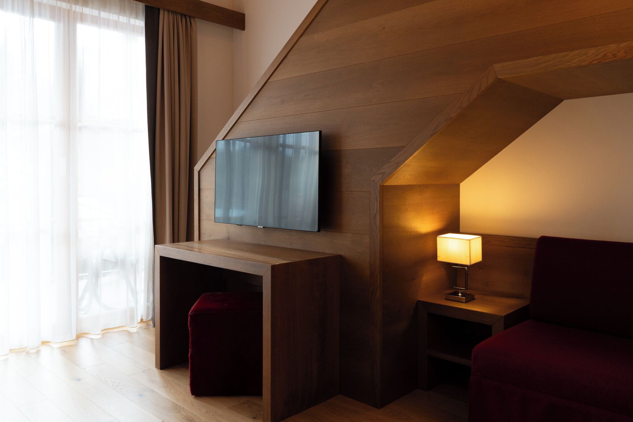Una camera moderna con una TV a schermo piatto montata su una parete in legno, un comodino con una lampada e una poltrona imbottita rossa.