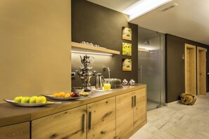 A modern kitchen with a wooden countertop, a coffee maker, fruit, and a glass door leading to a bathroom. - Hotel La Fradora - Dolomites Hotel (San Cassiano)