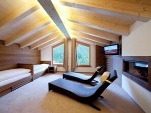 Une pièce mansardée chaleureuse, aménagée avec un lit, un fauteuil confortable, un téléviseur et une cheminée.
