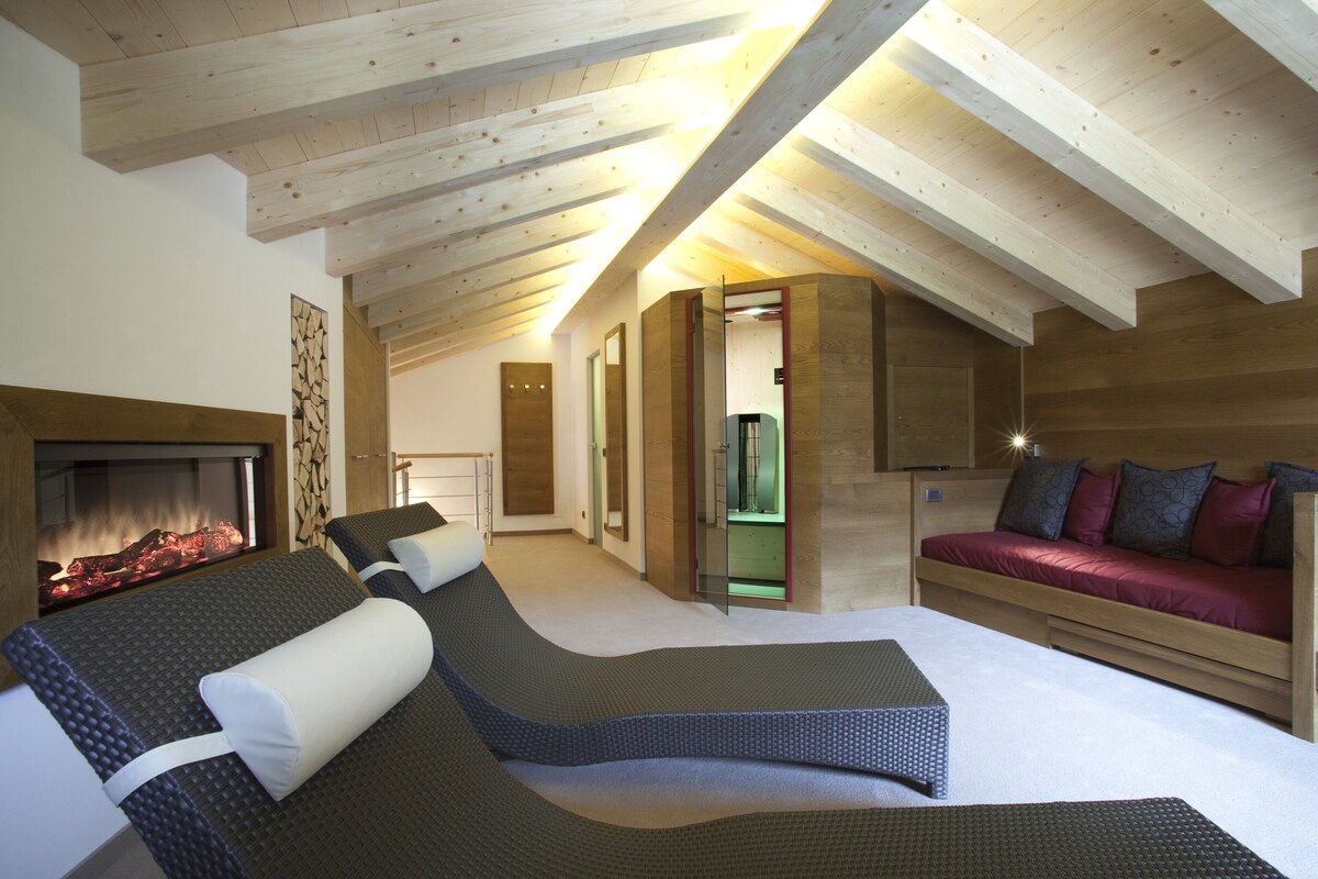 A high-ceilinged room with a fireplace, a sofa, and a bed with a view of the outdoors.