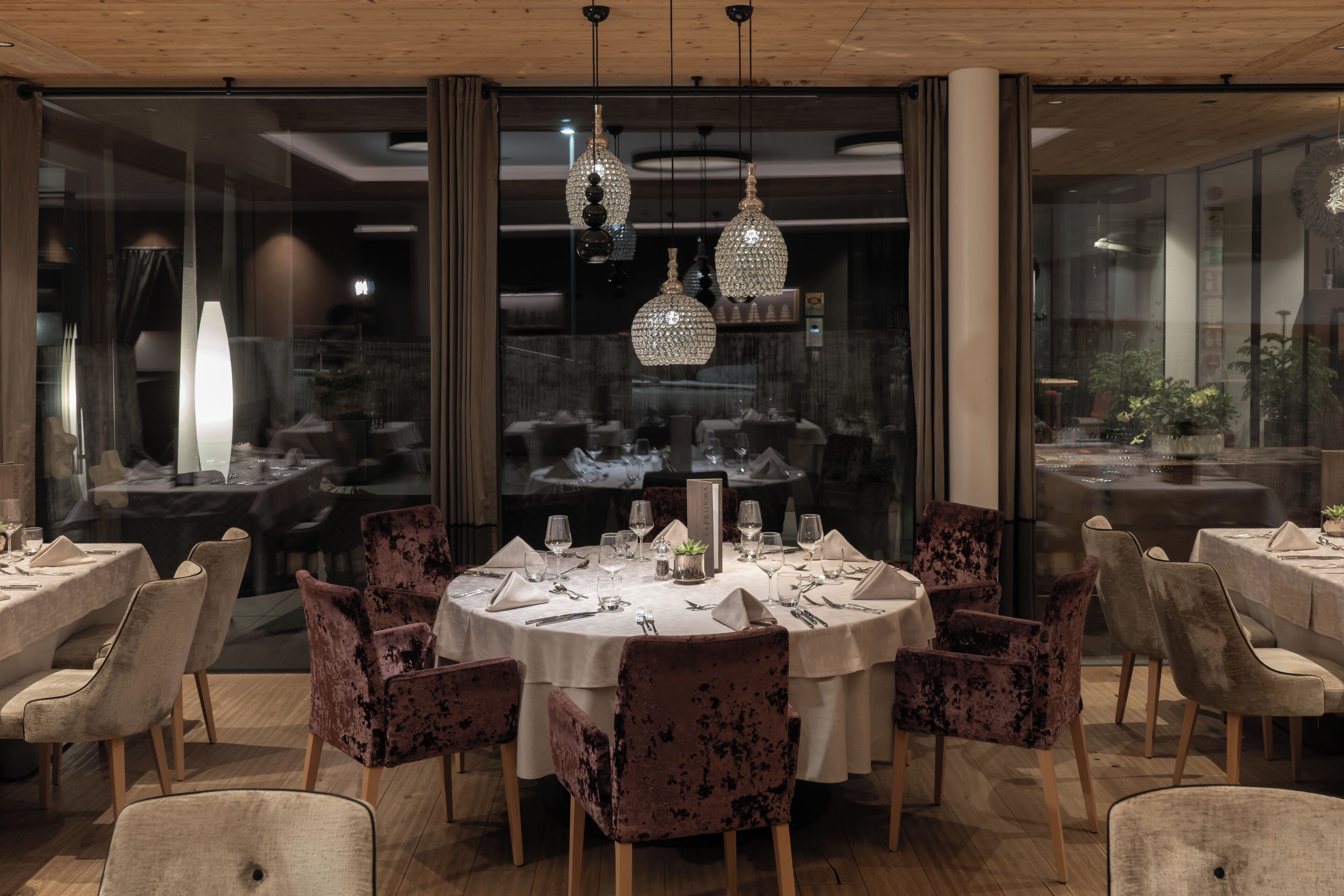 Zona pranzo con tavoli rotondi, sedie in velluto e lampadari di cristallo.