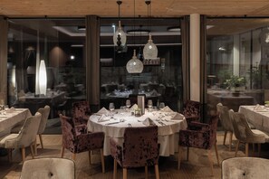 Un comedor con mesas redondas, sillas de terciopelo y candelabros de cristal.