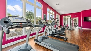 Un gimnasio con cintas de correr, elípticas y máquinas de pesas, ventanas amplias y una pared roja.