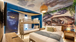 Quarto com beliches, escrivaninha, mural no teto e mesa de cabeceira com luminária.