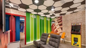 Um quarto com parede de tijolos, parede listrada em verde e branco, máquina de arcade Pac-Man e duas poltronas cinzentas.