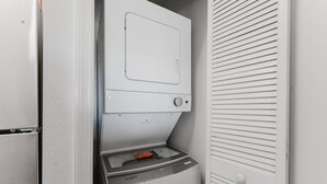 A compact laundry room with a front-loading washer and dryer, a small countertop, and a door with horizontal louvered panels. - Resort Suite on International Drive (Orlando)