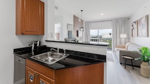 A modern kitchen with a black countertop, wooden cabinets, and a built-in dishwasher. - Resort Suite on International Drive (Orlando)