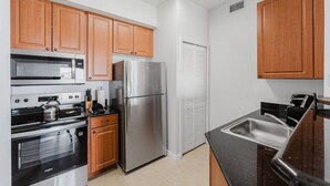A kitchen with wooden cabinets, stainless steel appliances, a black countertop, and a white door. - Resort Suite on International Drive (Orlando)