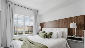 A modern hotel room with a large bed, a view of the city, and a wooden accent wall. - Resort Suite on International Drive (Orlando)