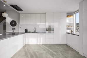 Eine moderne Küche mit weißen Schränken, einem eingebauten Backofen, einer Kaffeemaschine und einer Wanduhr.