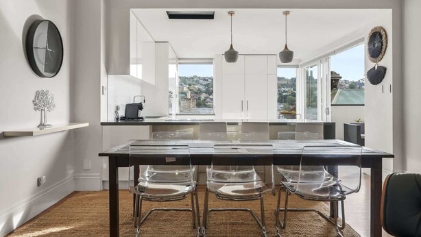 Une cuisine moderne dotée d’un grand îlot central, de chaises en verre transparent et offrant une vue sur la ville.