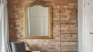 Une pièce avec un mur en briques, un grand miroir décoratif, un fauteuil avec des coussins et une porte.