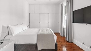 Une chambre à coucher avec un lit, une armoire, une télévision et une fenêtre avec des rideaux.