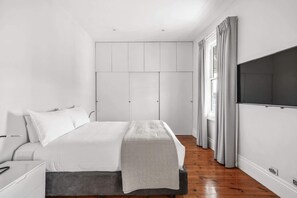 Ein Schlafzimmer mit Bett, Kleiderschrank, Fernseher und einem fenster mit Vorhängen.
