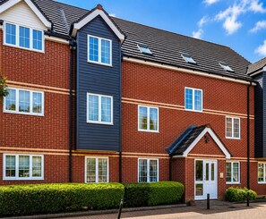 A multi-story residential building with a brick facade, multiple windows, and a small front garden. - Family Friendly 2-Bed Apartment with Patio, Garden Access & Parking (Newbury)