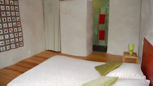 Ein Schlafzimmer mit einem Bett, einer Bilderwand, einer Tür und einem kleinen Tisch mit einer Lampe.