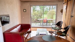 Ein Zimmer mit einer roten Ledersofa, einem Holzesstisch mit vier Stühlen, einem an der Wand befestigten Fernseher und einer Glastür, die auf eine Außenpatio mit Tisch und Stühlen führt.