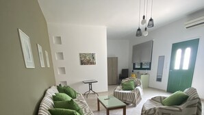 Ein Wohnzimmer mit zwei Sofas, einem Couchtisch, einem kleinen Tisch und einem Sessel. An der Wand hängt ein Gemälde und es gibt eine Tür mit einem Fenster.