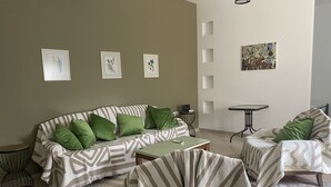 Ein Wohnzimmer mit einer Couch, zwei Sesseln, einem Couchtisch und einem kleinen Beistelltisch. An der Wand hängen gerahmte botanische Drucke und ein Gemälde.