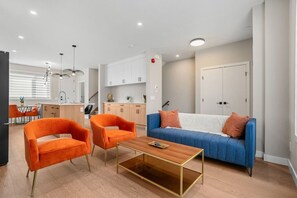Ein modernes Wohnzimmer mit einer Couch, zwei Sesseln, einem Couchtisch und einer Küche im Hintergrund.