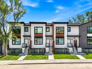 A modern multi-story residential building with a symmetrical facade, large windows, and a central staircase. - 2 King Bed | Garage | Min to UofC | NEW (Calgary)