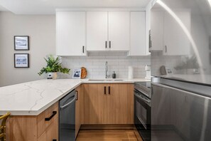 Eine moderne Küche mit weißen Schränken, einer Marmorarbeitsplatte, einem Geschirrspüler, einem Backofen und einem Kühlschrank.