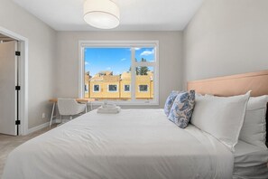 Ein Hotelzimmer mit einem großen Bett, einem Schreibtisch, einem Stuhl und einem Fenster mit Blick auf Gebäude.