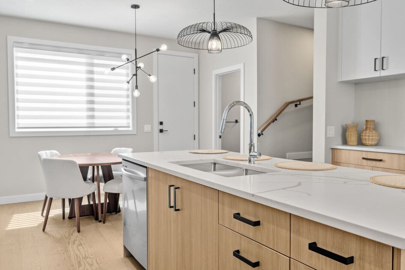 A modern kitchen with a central island, a dining area with chairs, and a staircase.