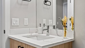 Ein modernes Badezimmer mit einem weißen Marmorwaschbecken, einem Chromarmaturen und einem Spiegel, der eine Vase mit Blumen reflektiert.