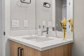 Ein modernes Badezimmer mit einem weißen Marmorwaschbecken, einem Chromarmaturen und einem Spiegel, der eine Vase mit Blumen reflektiert.