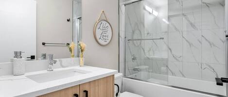 Ein modernes Badezimmer mit Duschkabine aus Glas, einer weißen Toilette und einem Waschtisch mit Marmorplatte.