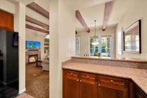 A kitchen with wooden cabinets, a granite countertop, and a fireplace. - Desert Serenity #A - 1 BR Legacy Villas (La Quinta)