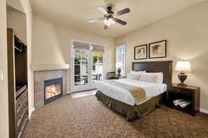 Habitación de hotel con cama, chimenea, ventilador de techo y vistas a través de un ventanal.