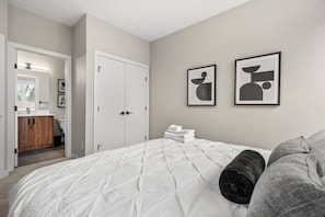 Ein Schlafzimmer mit Bett, Kleiderschrank, Badezimmer und zwei gerahmten Kunstwerken an der Wand.