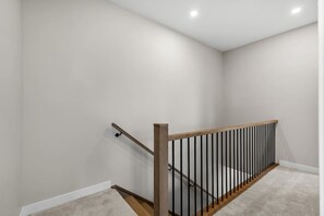 Eine Treppe mit hölzernem Geländer und schwarzen Spindeln, mit Teppich belegten Stufen und weißen Wänden.