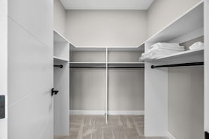 Ein begehbarer Kleiderschrank mit weißen Wänden, einer zentralen Kleiderstange und einem Teppichboden.